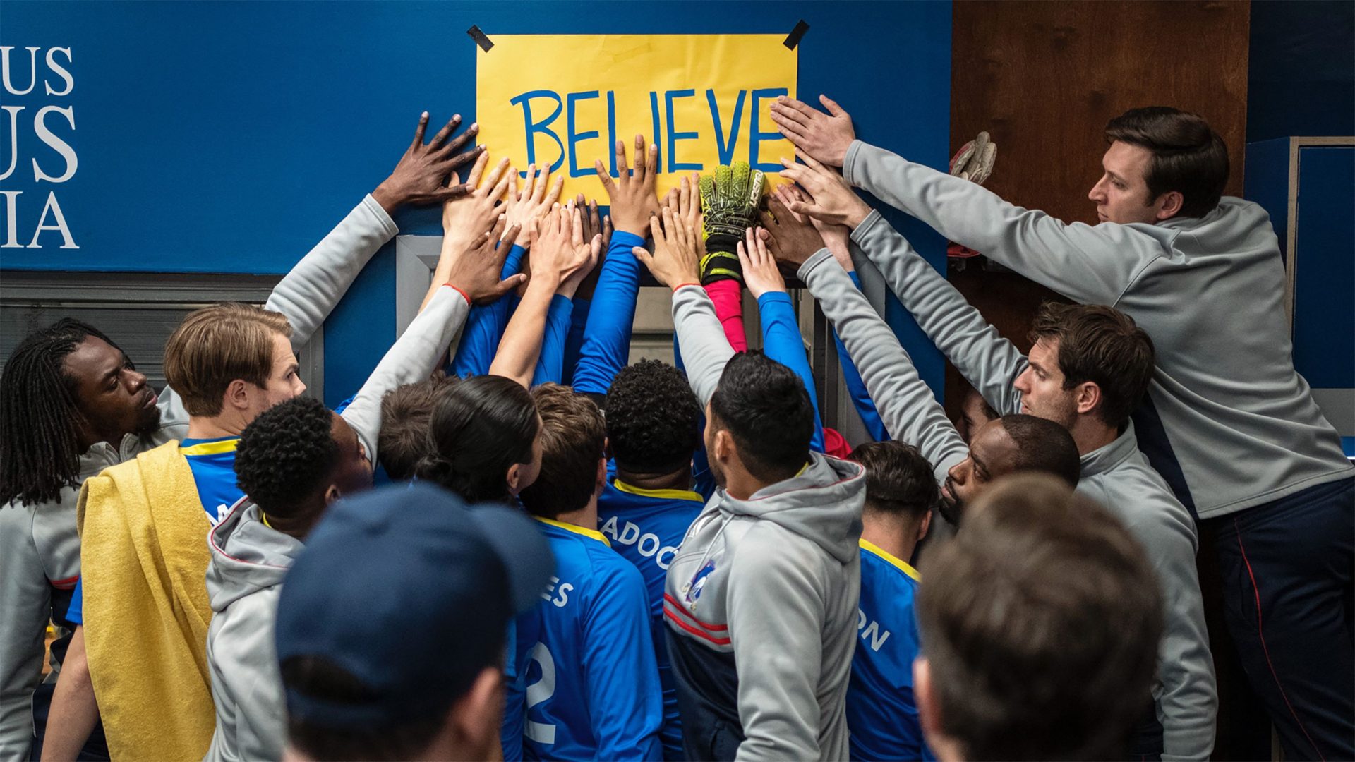 The squad of AFC Richmond from Ted Lasso, place their hands on a sign reading 'Believe'