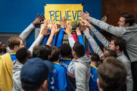 The squad of AFC Richmond from Ted Lasso, place their hands on a sign reading 'Believe'